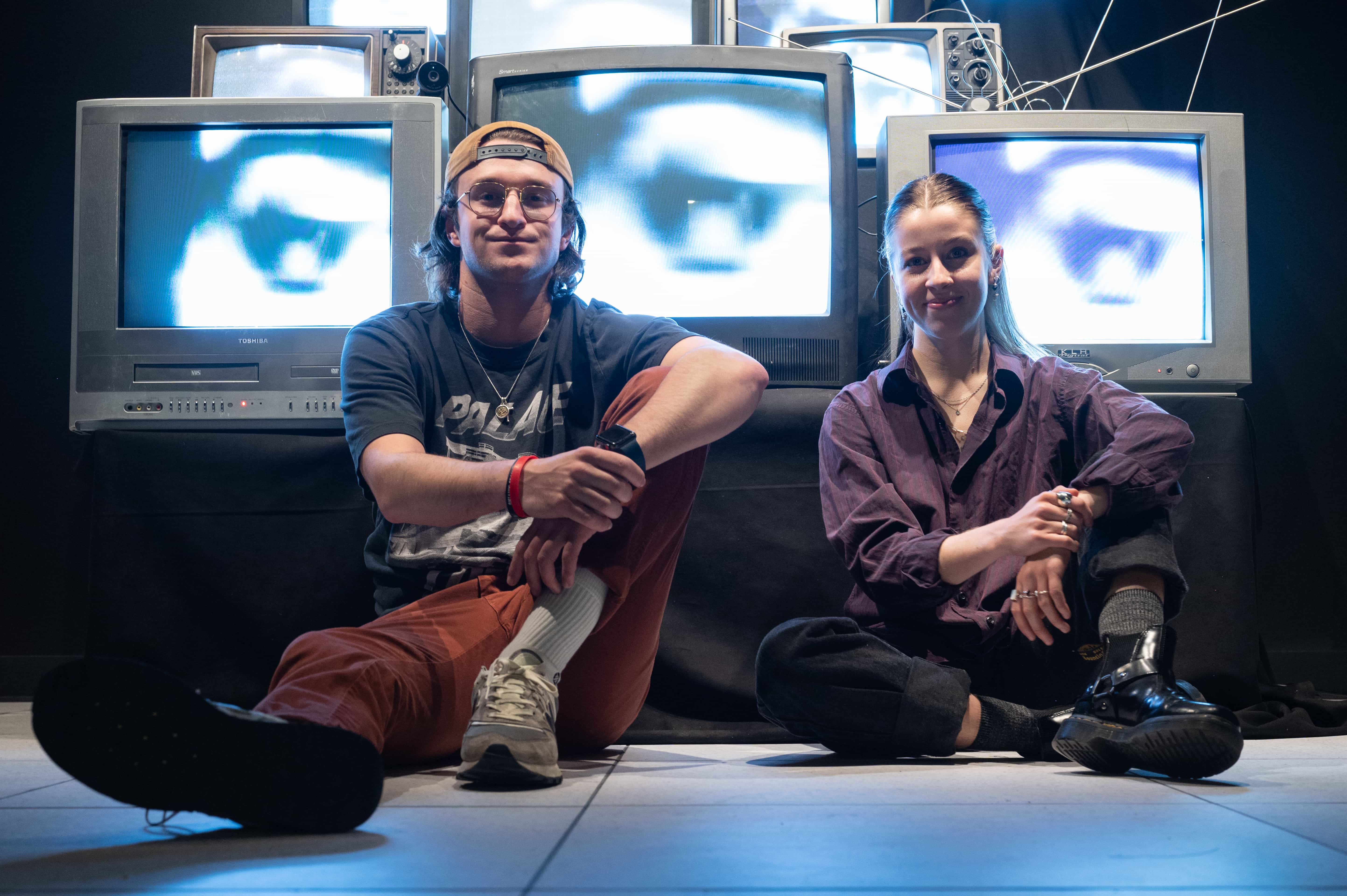 Two Spect project collaborators seated in front of stacked CRT televisions showing glowing eye imagery.